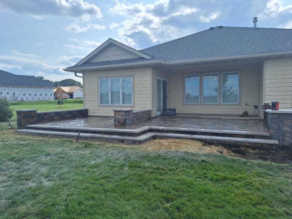 Newly constructed patio with stone accents at a residential home, surrounded by green lawn.