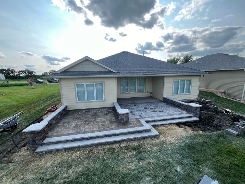 Newly constructed home exterior with stone patio and landscaped yard, under a cloudy sky.
