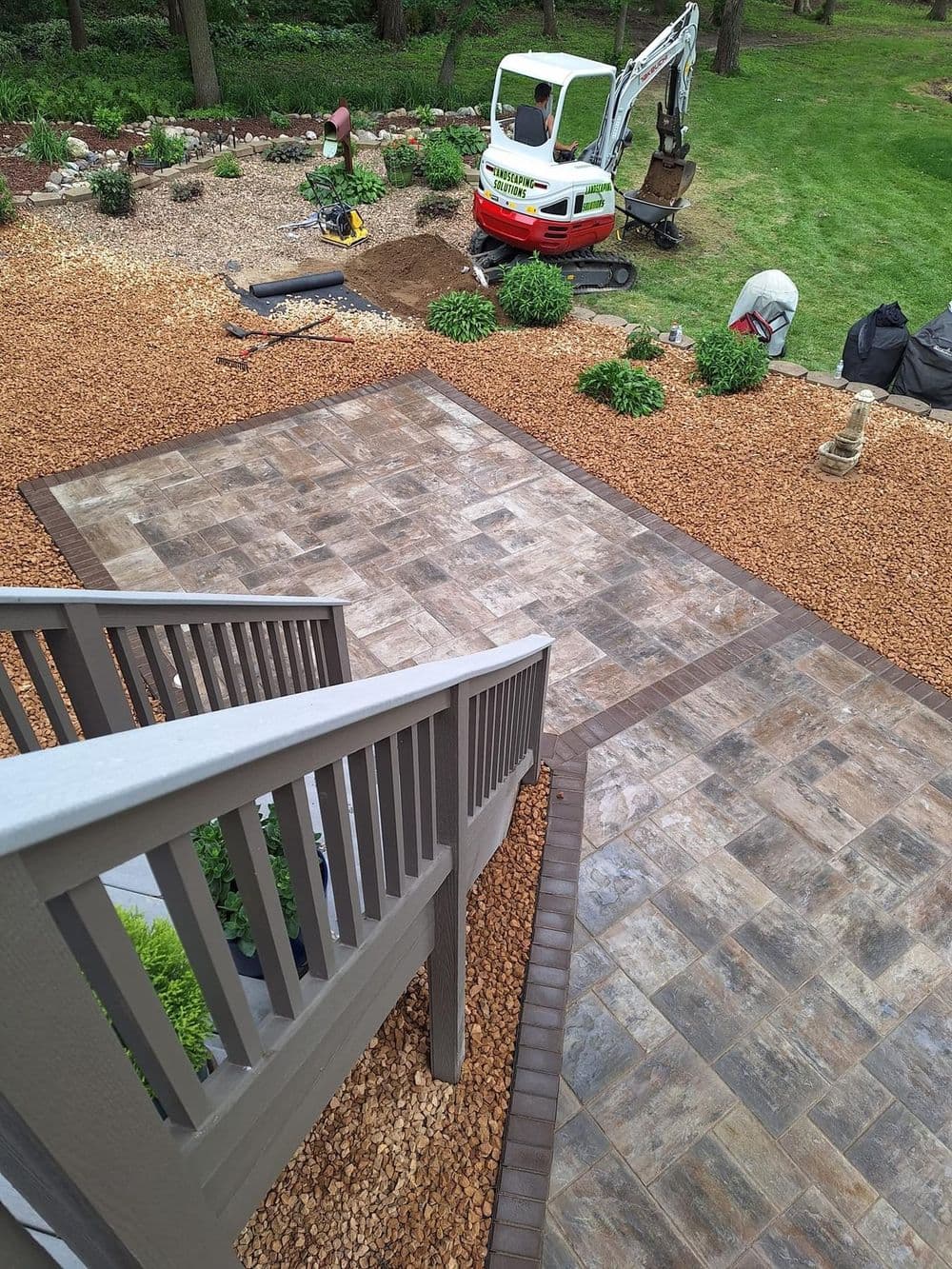 Construction site showcasing a landscaped garden with a stone patio and machinery in use.