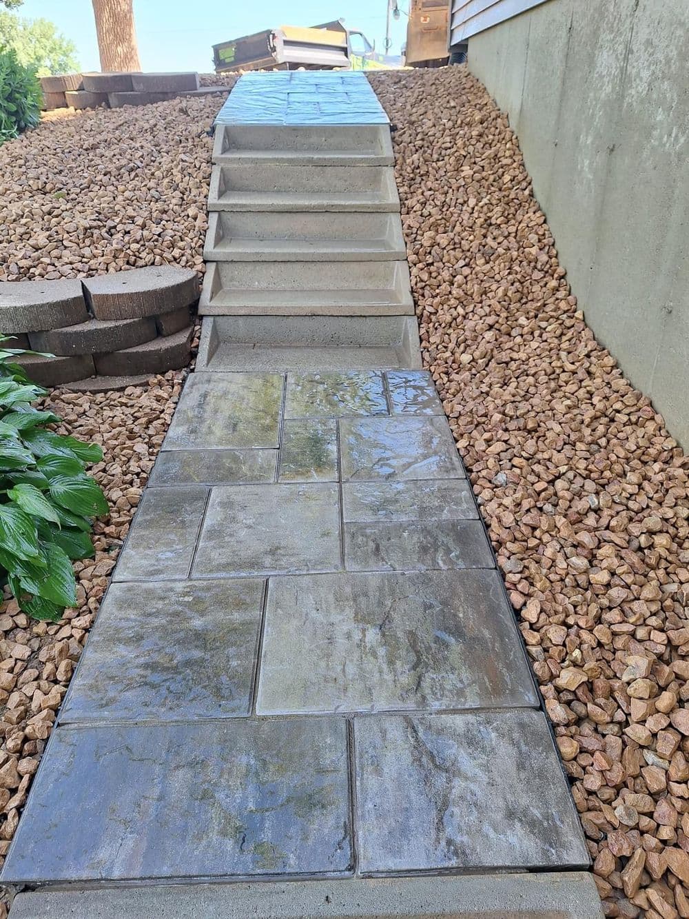Stone pathway with steps leading up to a house, surrounded by gravel and greenery.