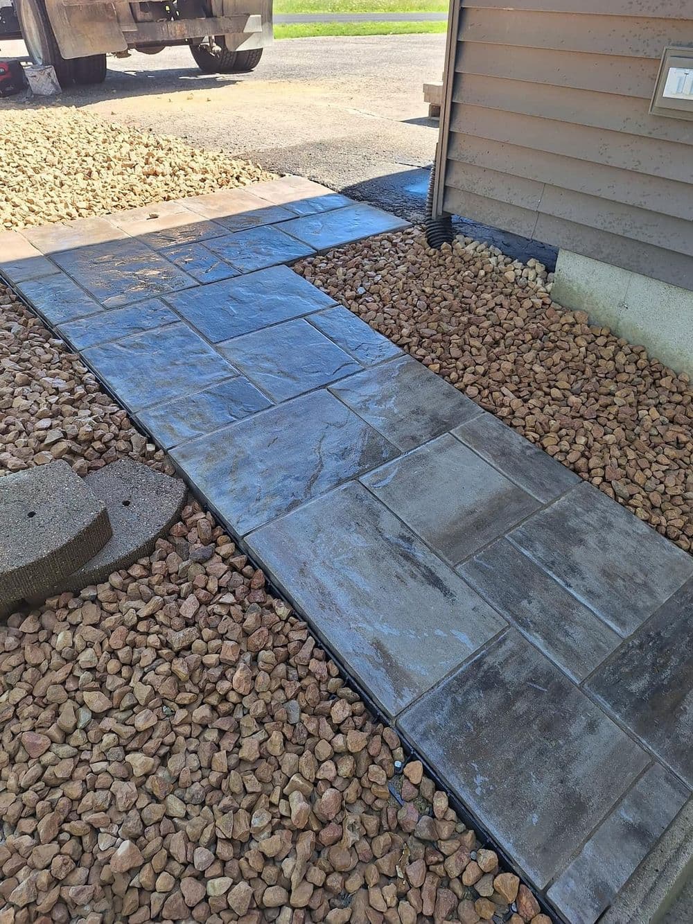 Newly laid concrete walkway beside a house, surrounded by decorative gravel.