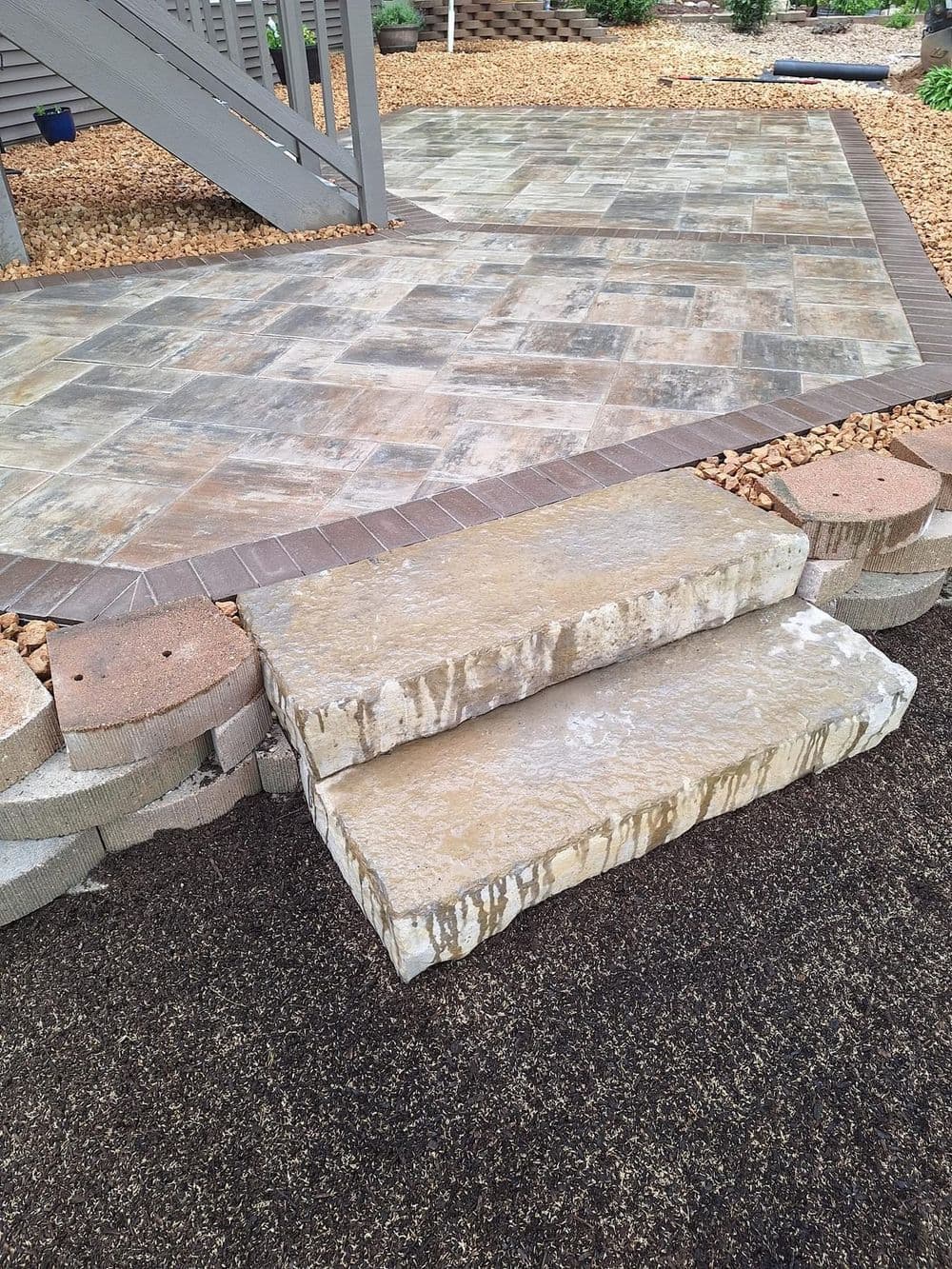 Stone steps leading up to a patio area with textured stone tiles and gravel landscaping.