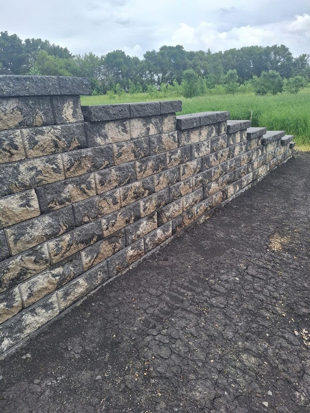 Stacked stone wall with gray and tan blocks, set against a green landscape.