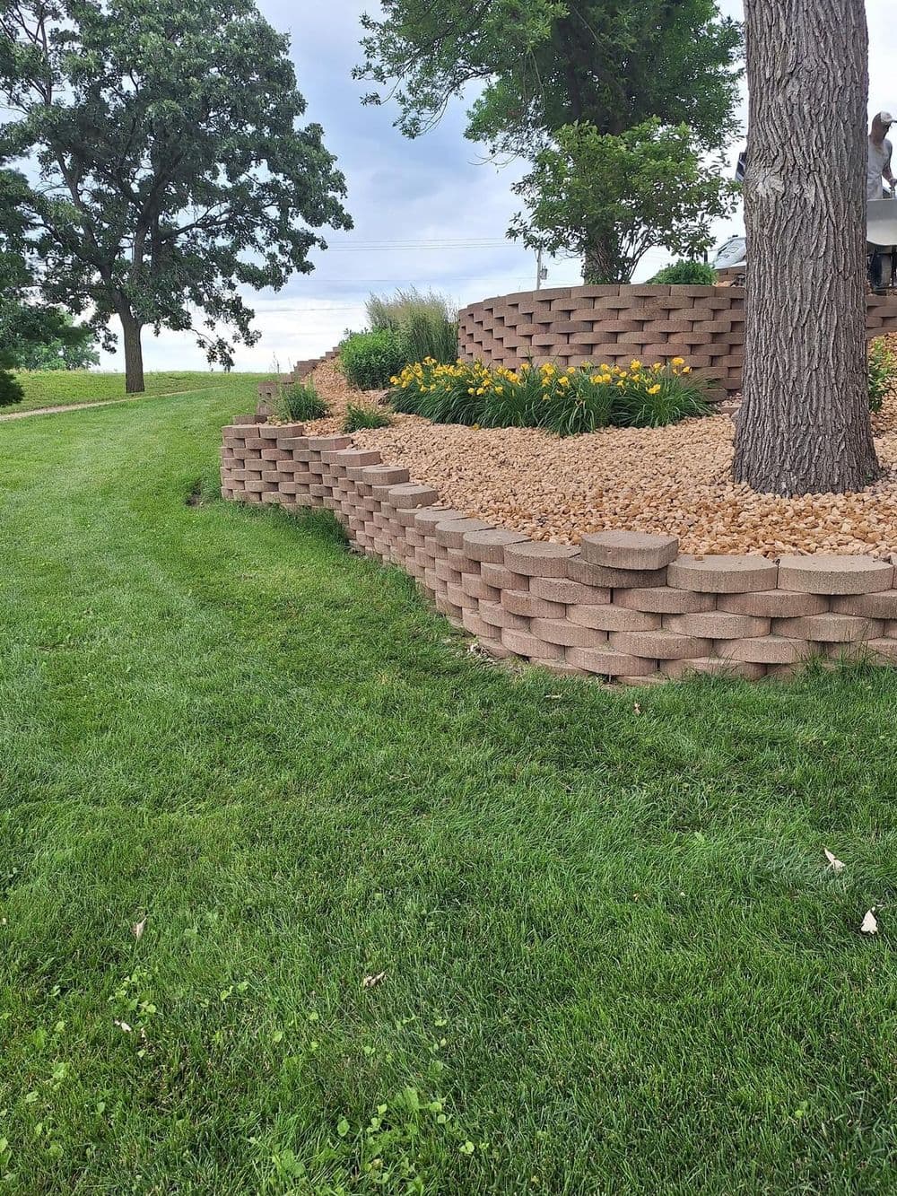 Landscaped garden with stone retaining walls, colorful flowers, and lush green grass.