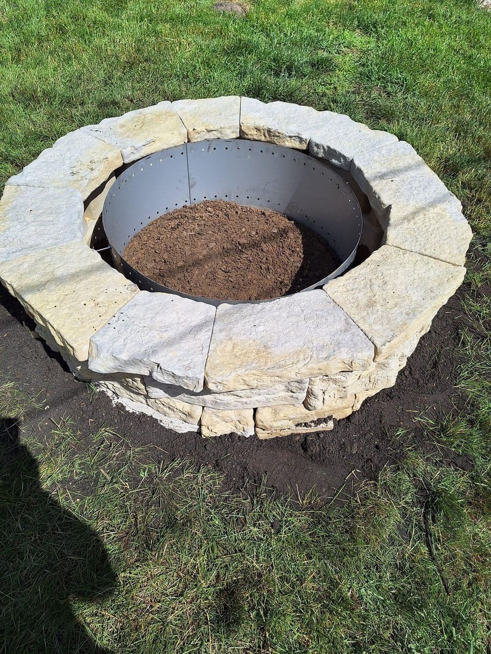 Stone fire pit under construction with a circular metal liner and soil in the center.