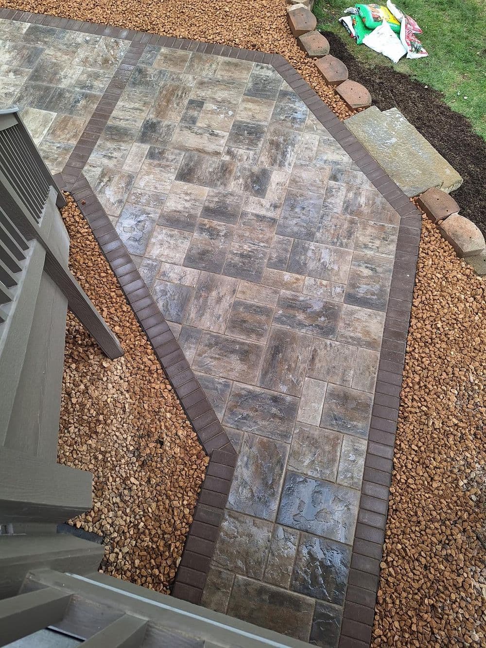 Paved walkway with gray stone tiles bordered by brown bricks and surrounded by gravel.