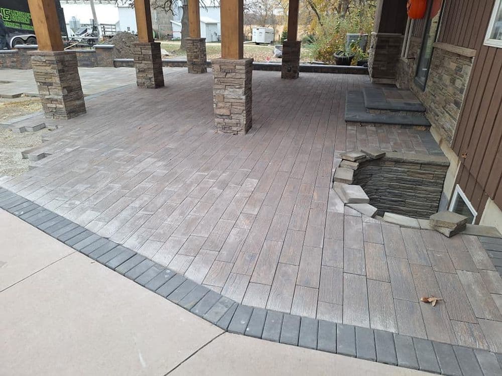 Paved patio with stone pillars and a missing section revealing a rock foundation.