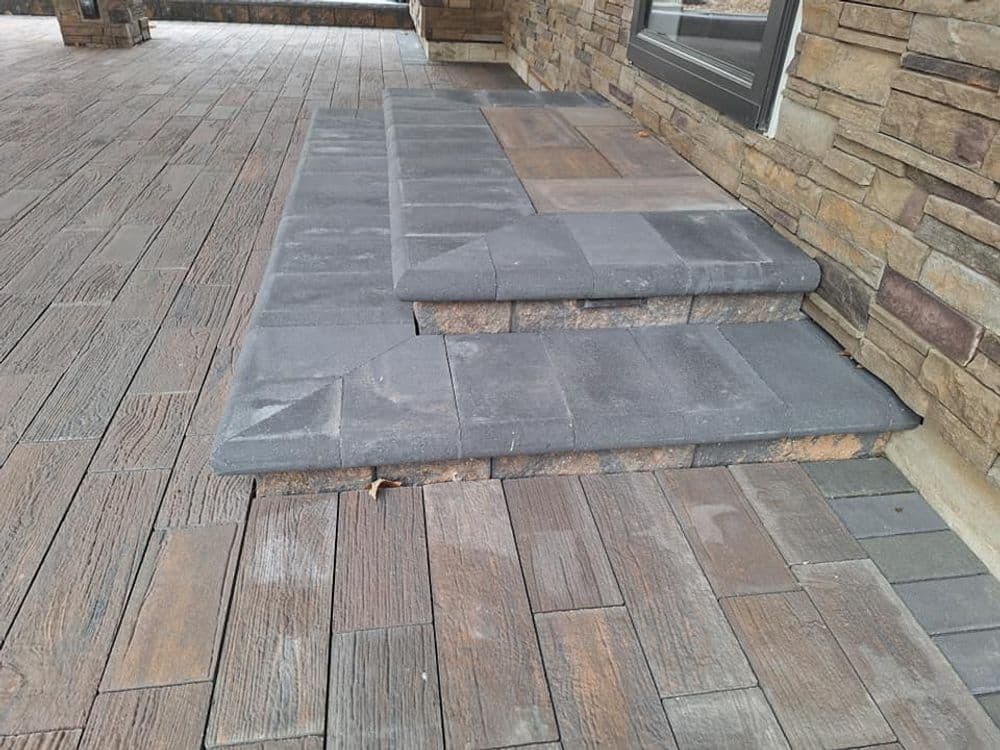 Gray stone steps leading to a house with textured wooden-style paving.