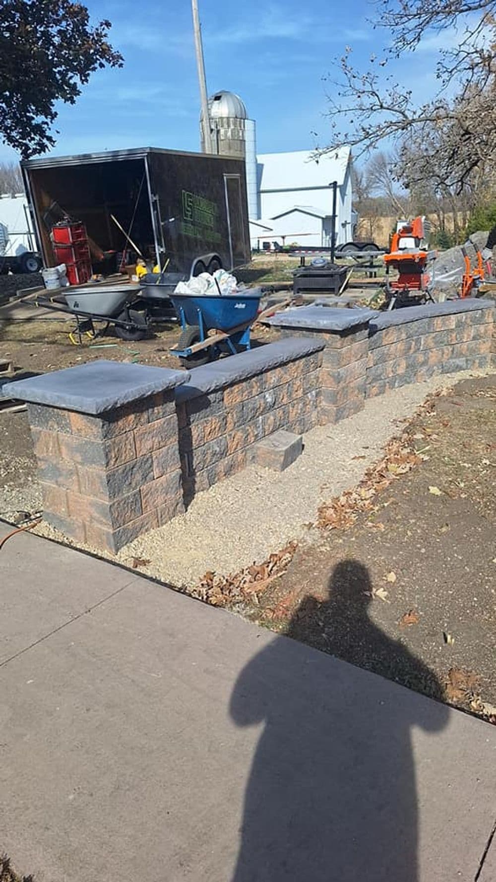Construction area with stone wall, wheelbarrows, and tools under blue sky.