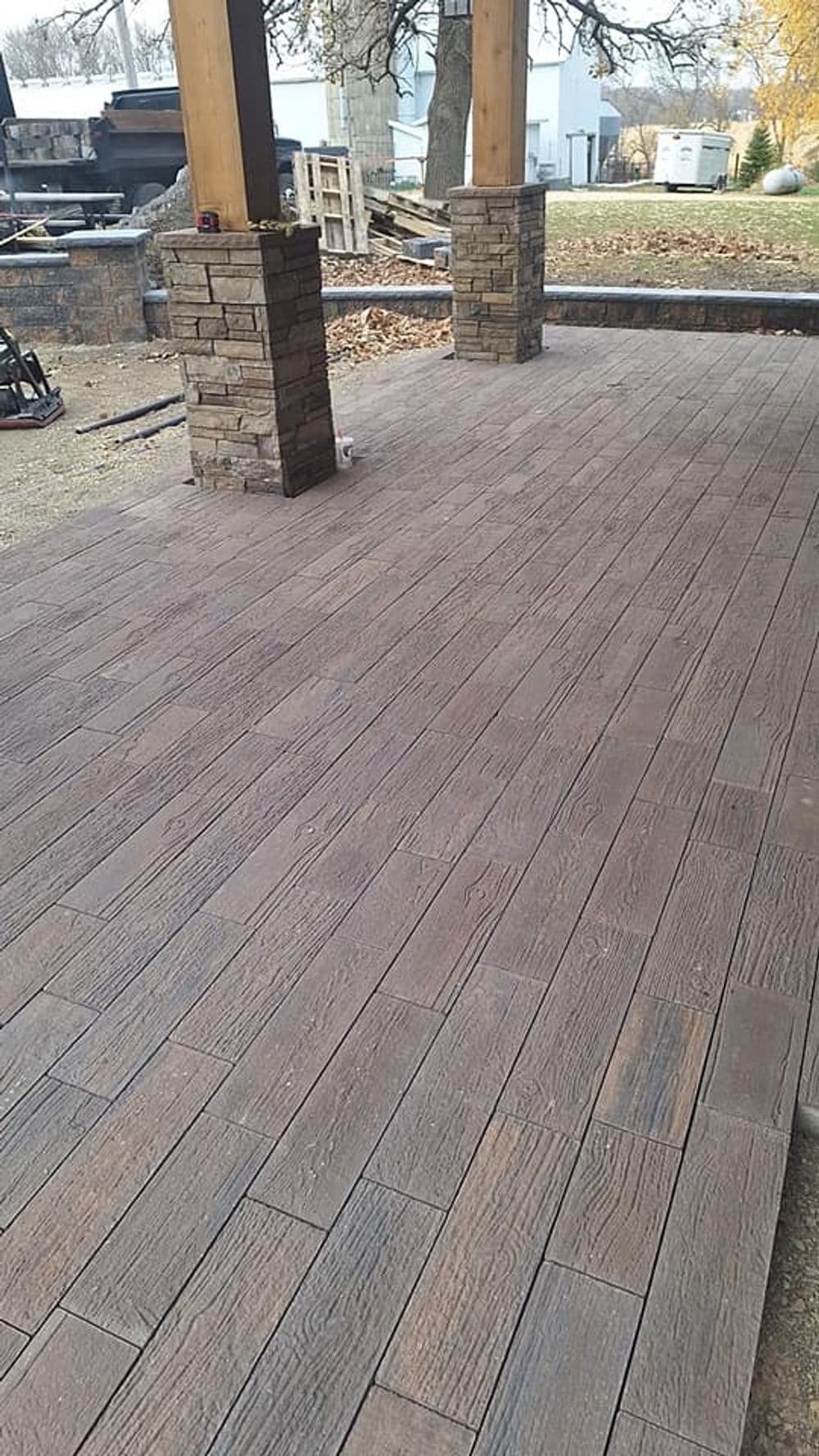 Newly installed wooden-look patio flooring with stone columns, surrounded by autumn scenery.