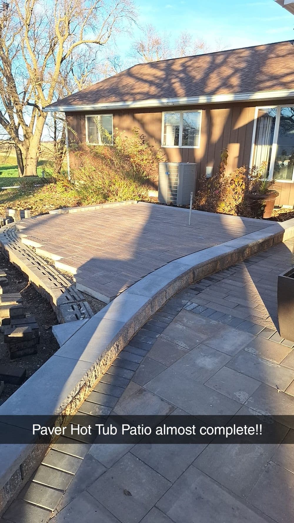 Paver hot tub patio nearing completion with curved brick design and sunny exterior.